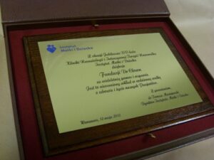 Dyplom grawerowany w mosiądzu złotym umieszczony na desce drewnianej w etui
